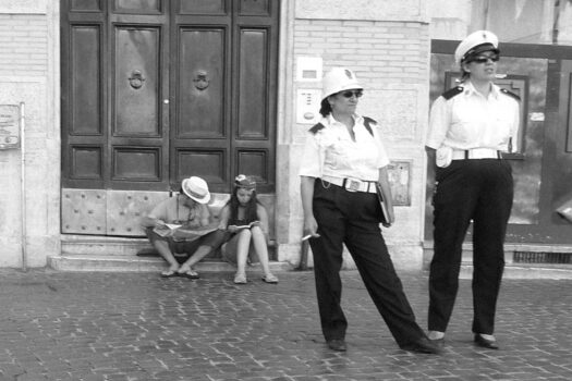 zwei italienische Polizistinnen stehen vor einer Kirchentür. Im Hintergrund auf der Stufe Touristen mit Kamera